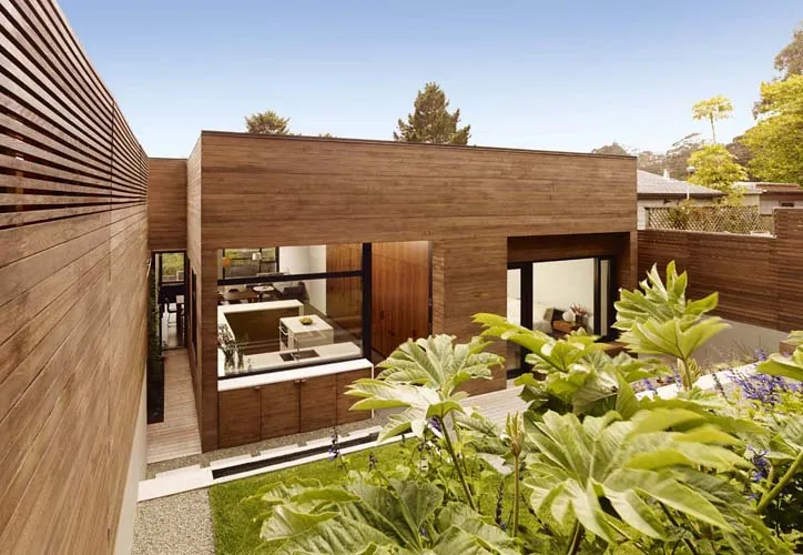 Exterior courtyard view of a modern flat-roofed house with extensive wood siding and large black-framed windows.