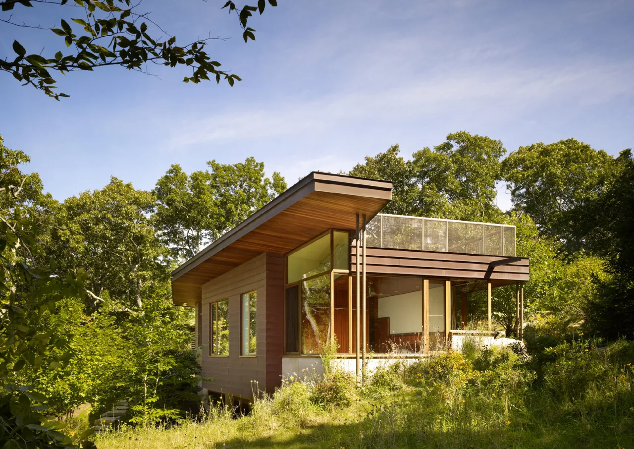 Exterior view of a modern guest house with a flat roof and large windows surrounded by greenery.