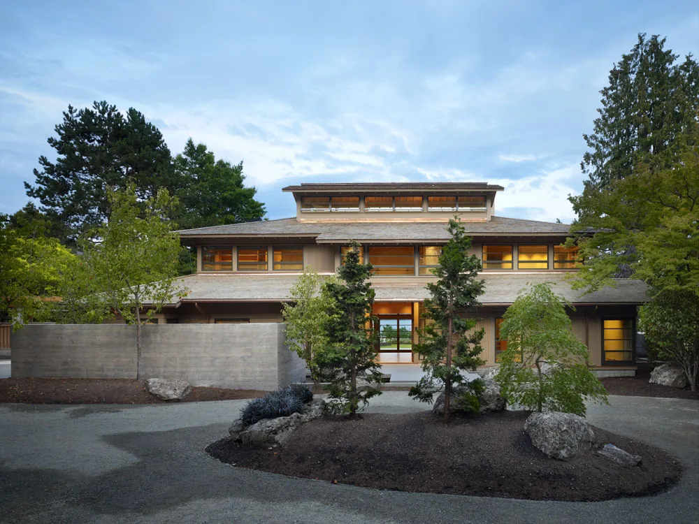 Front exterior view of a two-story house with tiered roof and multiple windows, surrounded by trees and landscaping.