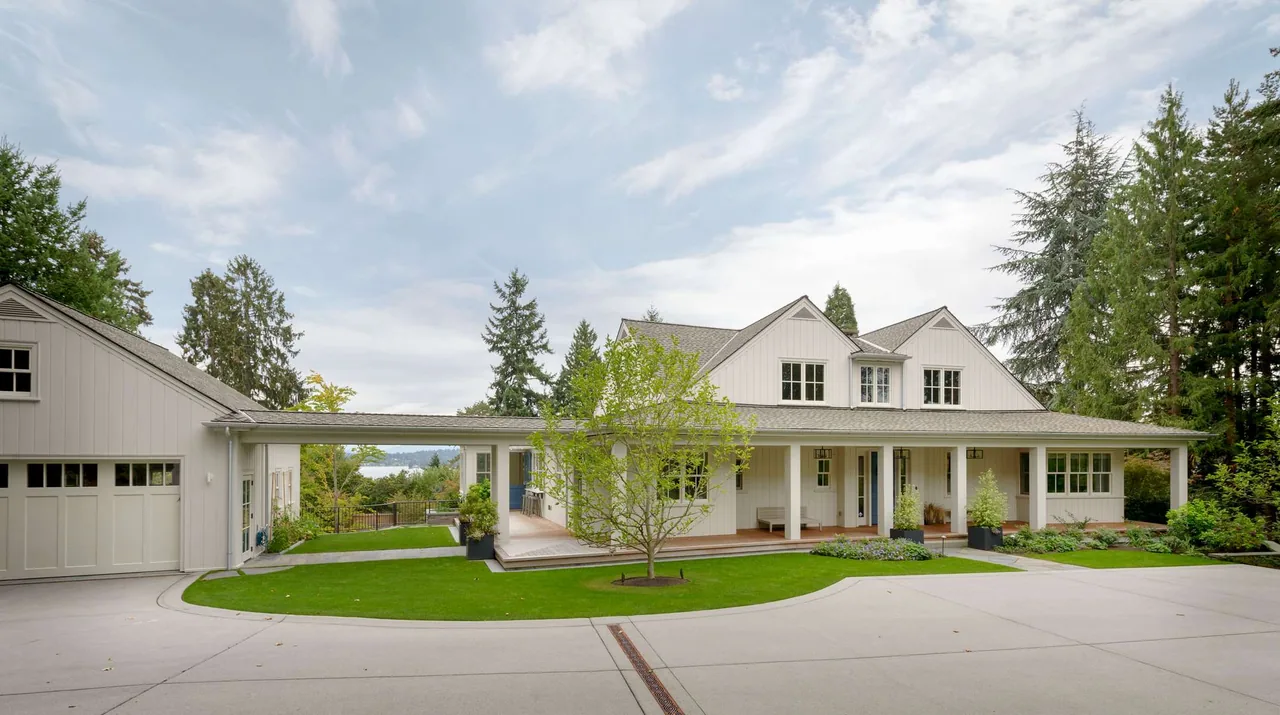 Front exterior of a modern farmhouse with white wood siding, a covered porch, and attached garage under a partly cloudy sky.