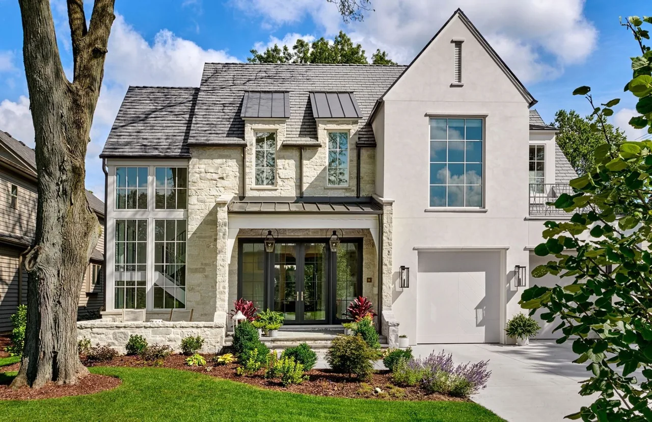 Front exterior of a two-story transitional residence with stone and stucco facade, a steep gable roof, and large windows.
