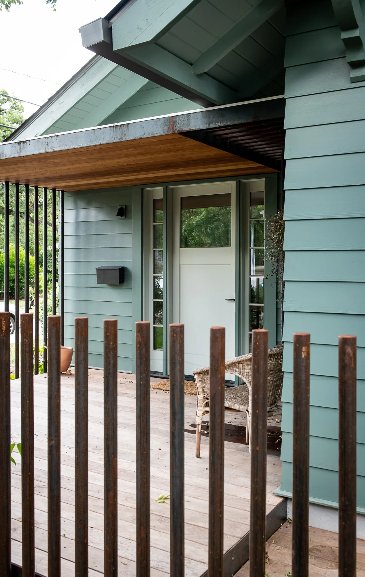 Front porch with wooden deck and a pale green house exterior featuring a white front door and vertical metal railing.