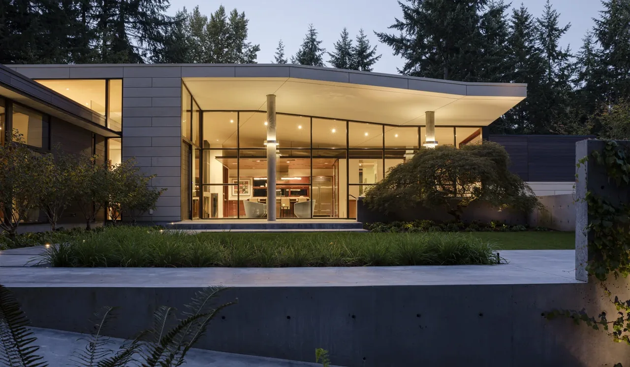 Exterior view of Inside Outside House at dusk showing large glass walls and a flat roof.