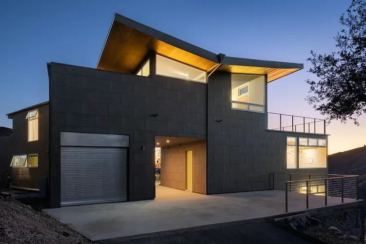 Exterior view of a modern two-story house at dusk with illuminated windows and a cantilevered roof.