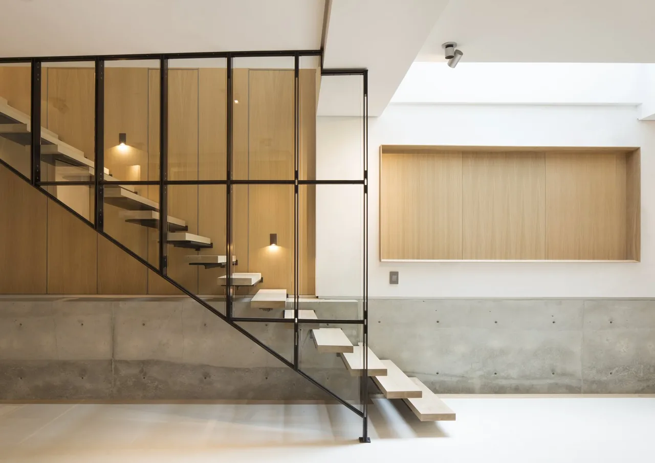 Minimalist interior with floating stairs, black window frames, and wood paneling on the wall.