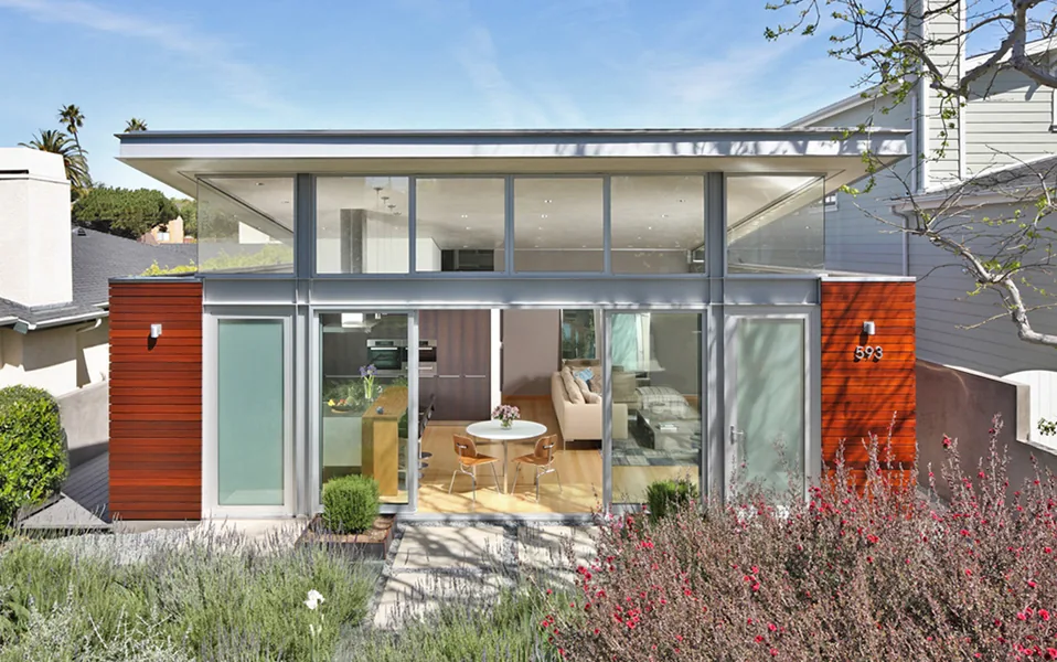 Modern home exterior with large glass doors and upper clerestory windows, featuring wood siding and a flat roof under a clear sky.