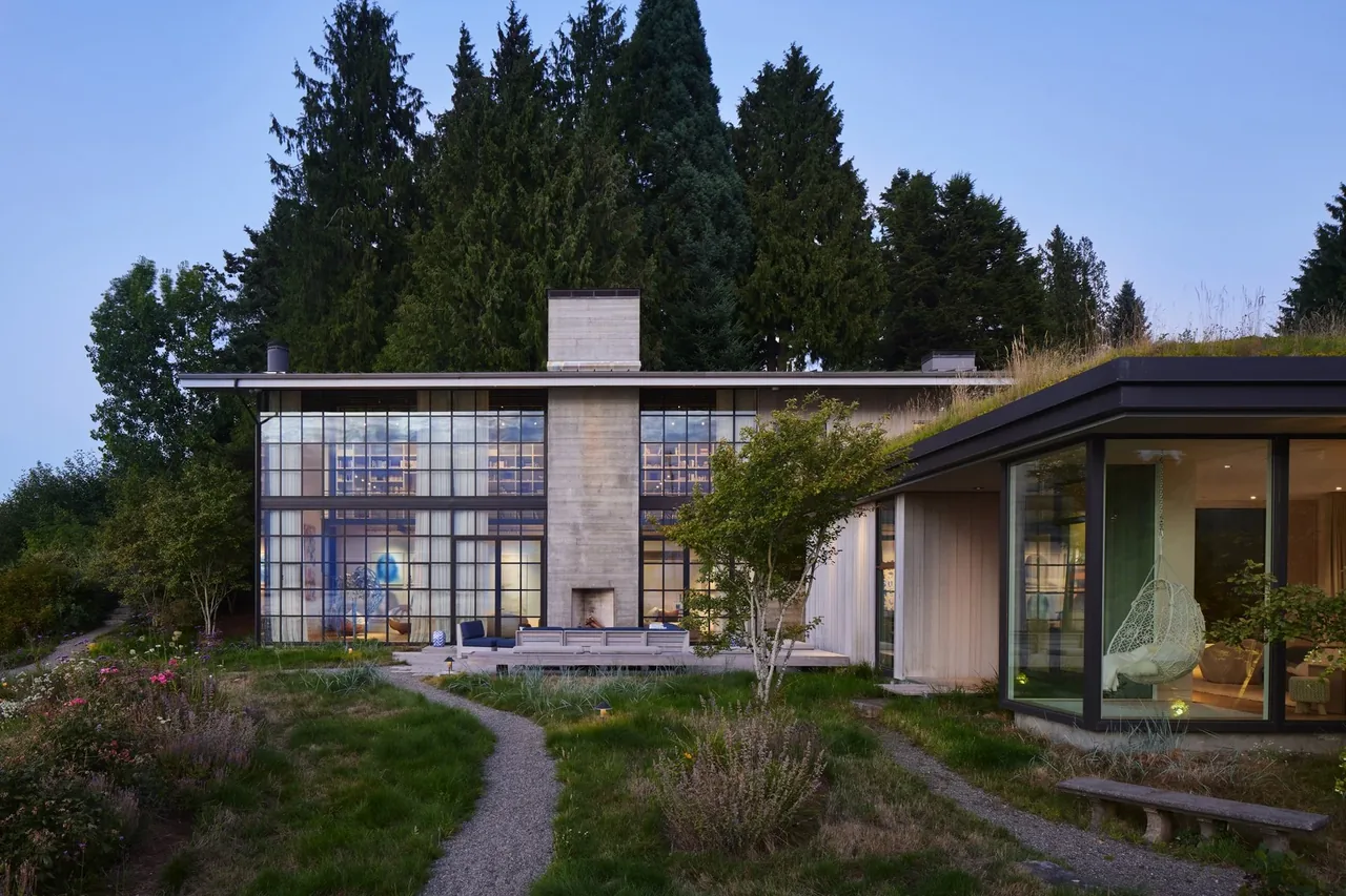 Two modern residential buildings surrounded by tall trees and landscaped grounds at dusk.