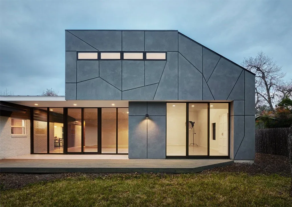 Modern two-story house exterior with geometric patterned gray panels and large black-framed windows at dusk.