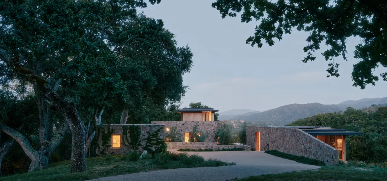 Stone villa exterior at dusk with natural stone walls and surrounding trees and hills.