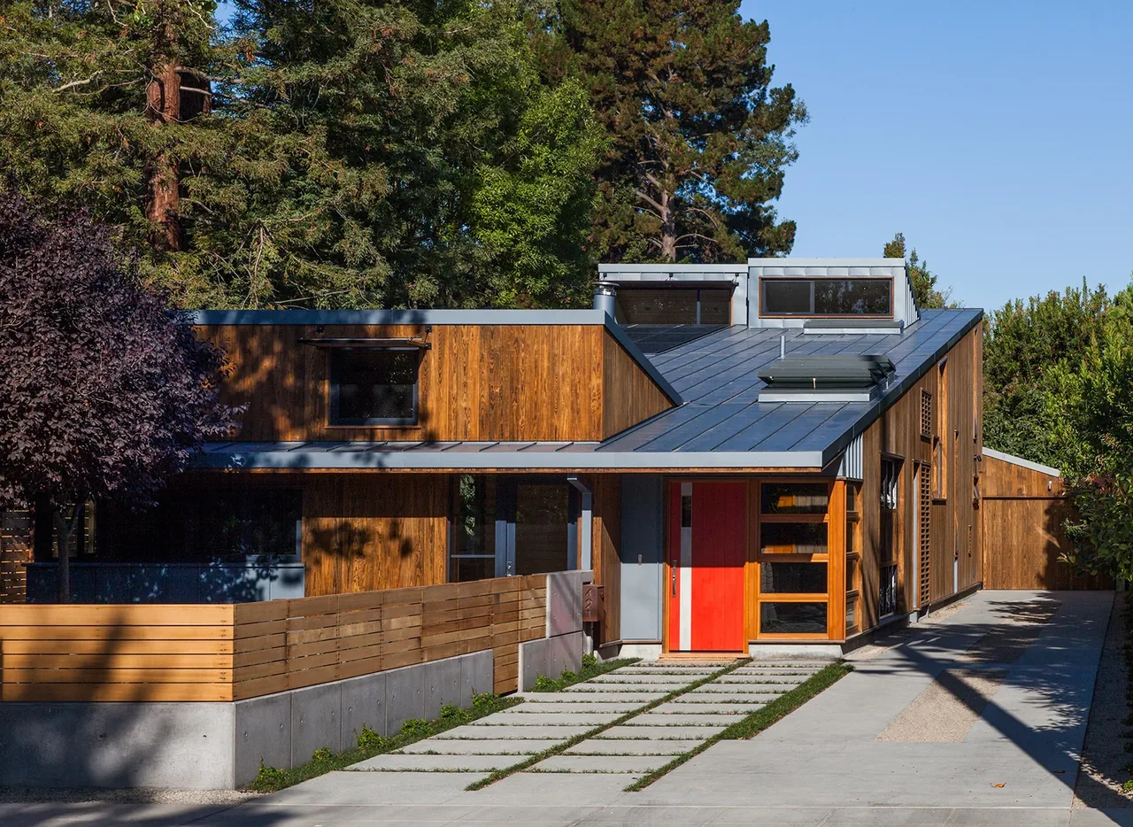 Modern house with wood siding, metal roof, and a bright red front door under clear blue sky.