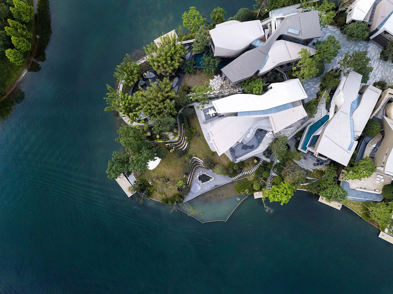 Aerial view of multiple modern lakeside villas with angular roofs and landscaped grounds surrounded by water.