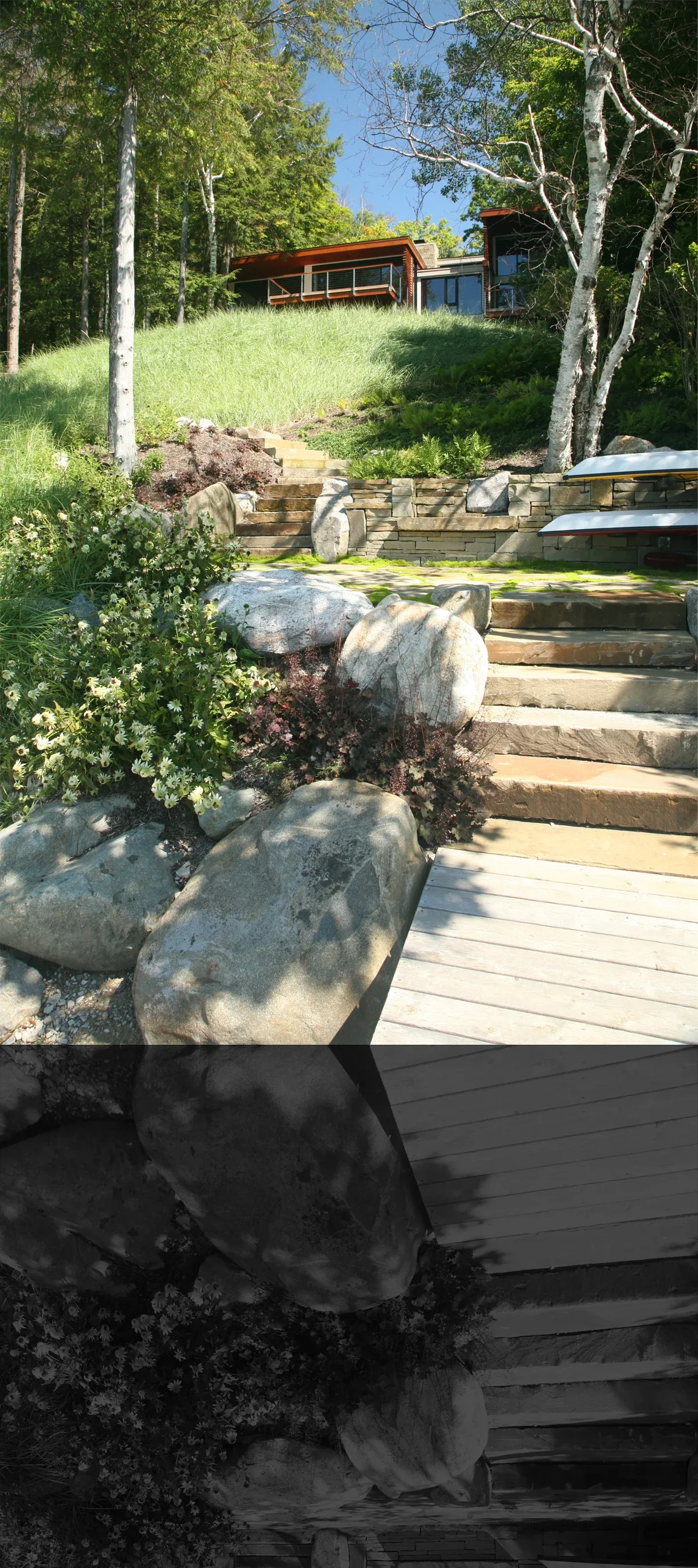 Stone steps leading up a hillside to a modern house surrounded by trees and greenery under a blue sky.