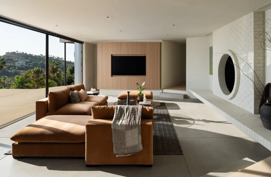 Living room with tan sectional sofa facing a built-in TV and a white brick fireplace with a circular opening, large sliding glass doors open