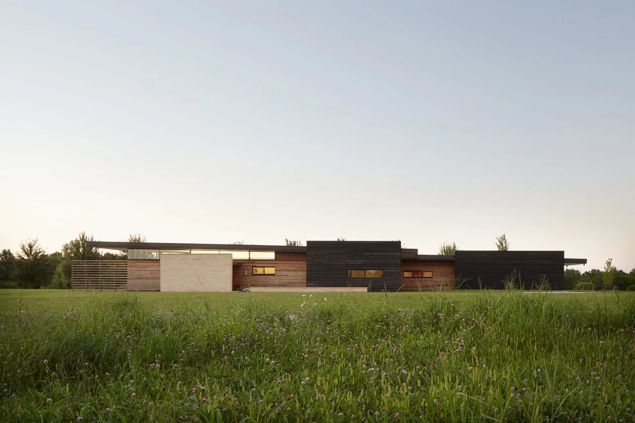 Low, modern horizontal house with mixed wood and dark panel exterior against a clear sky background.