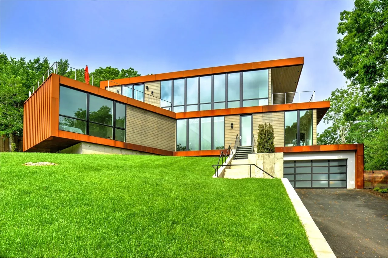 Modern home with large glass windows, rust-colored steel framing, and a garage built into a green grassy hill.