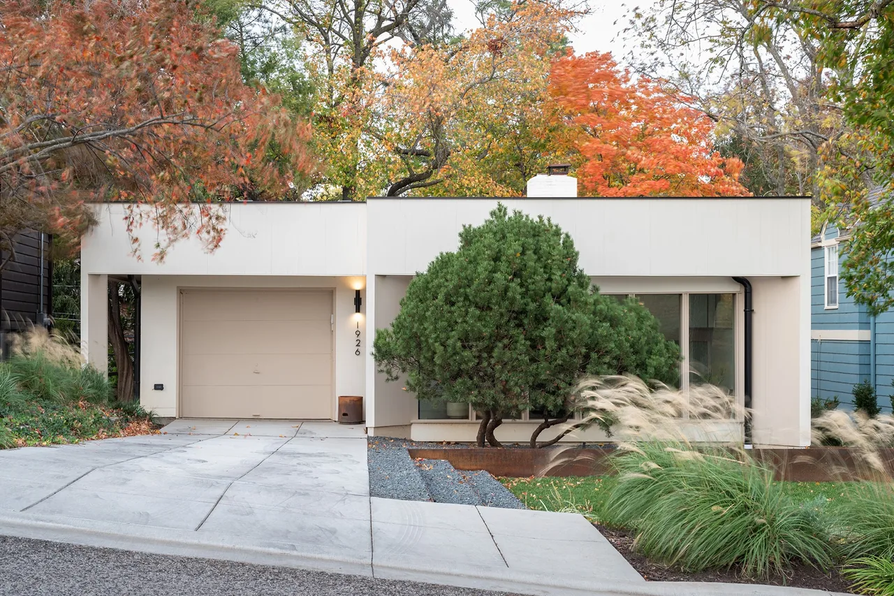 Modern one-story house with a flat roof, a garage, and a distinctive round tree in front during autumn.