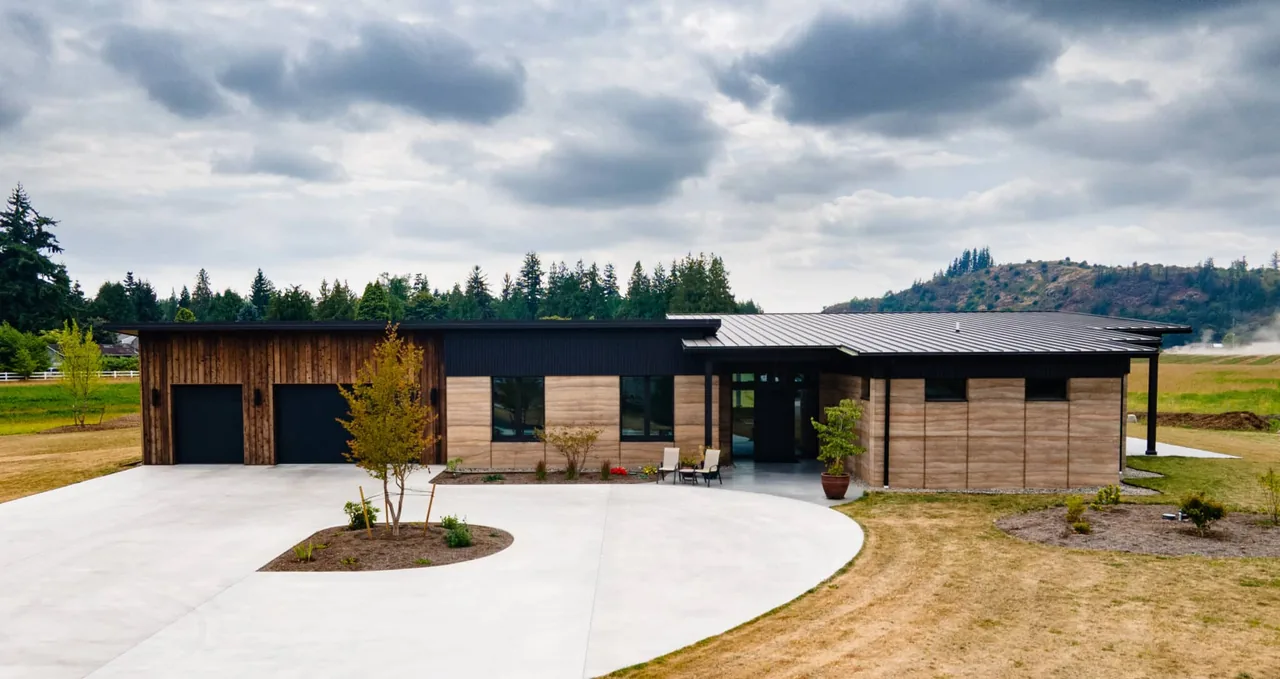 Single-story modern house with a flat and shed roof, featuring wood and concrete exterior and large driveway.