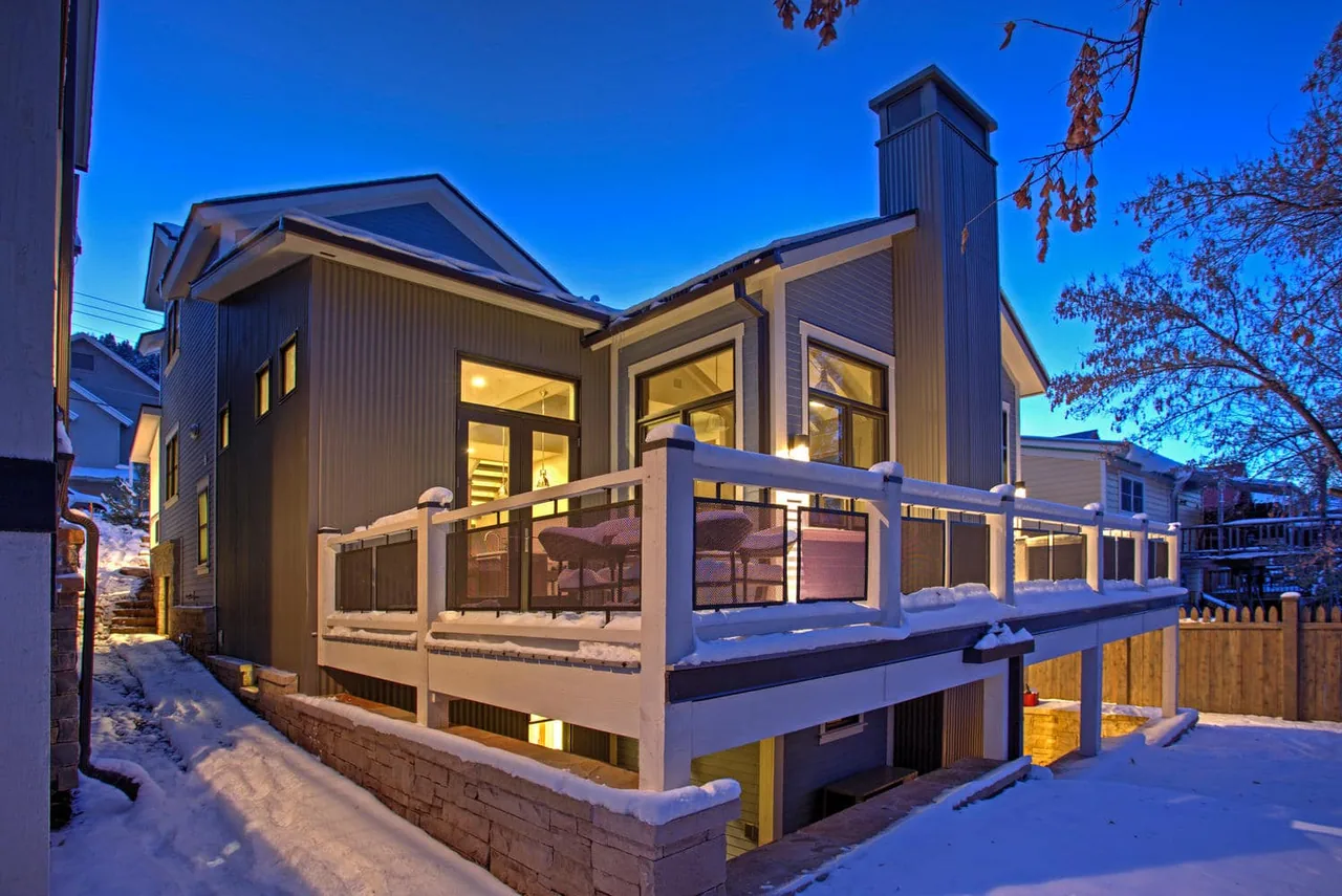 Rear exterior view of a modern two-story house with a raised balcony and glass door at dusk.