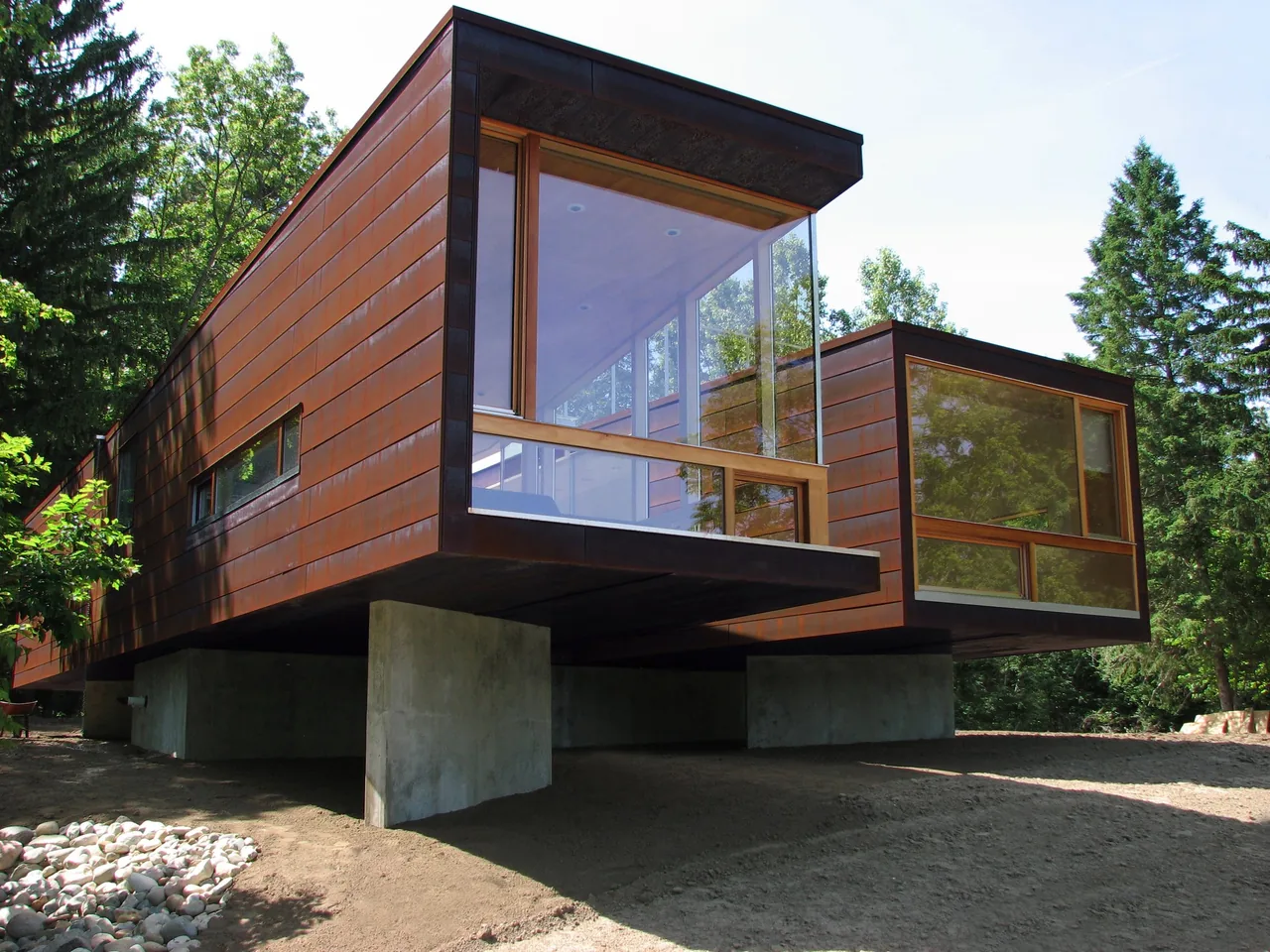 Modern elevated house with cantilevered sections and large corner windows surrounded by trees.