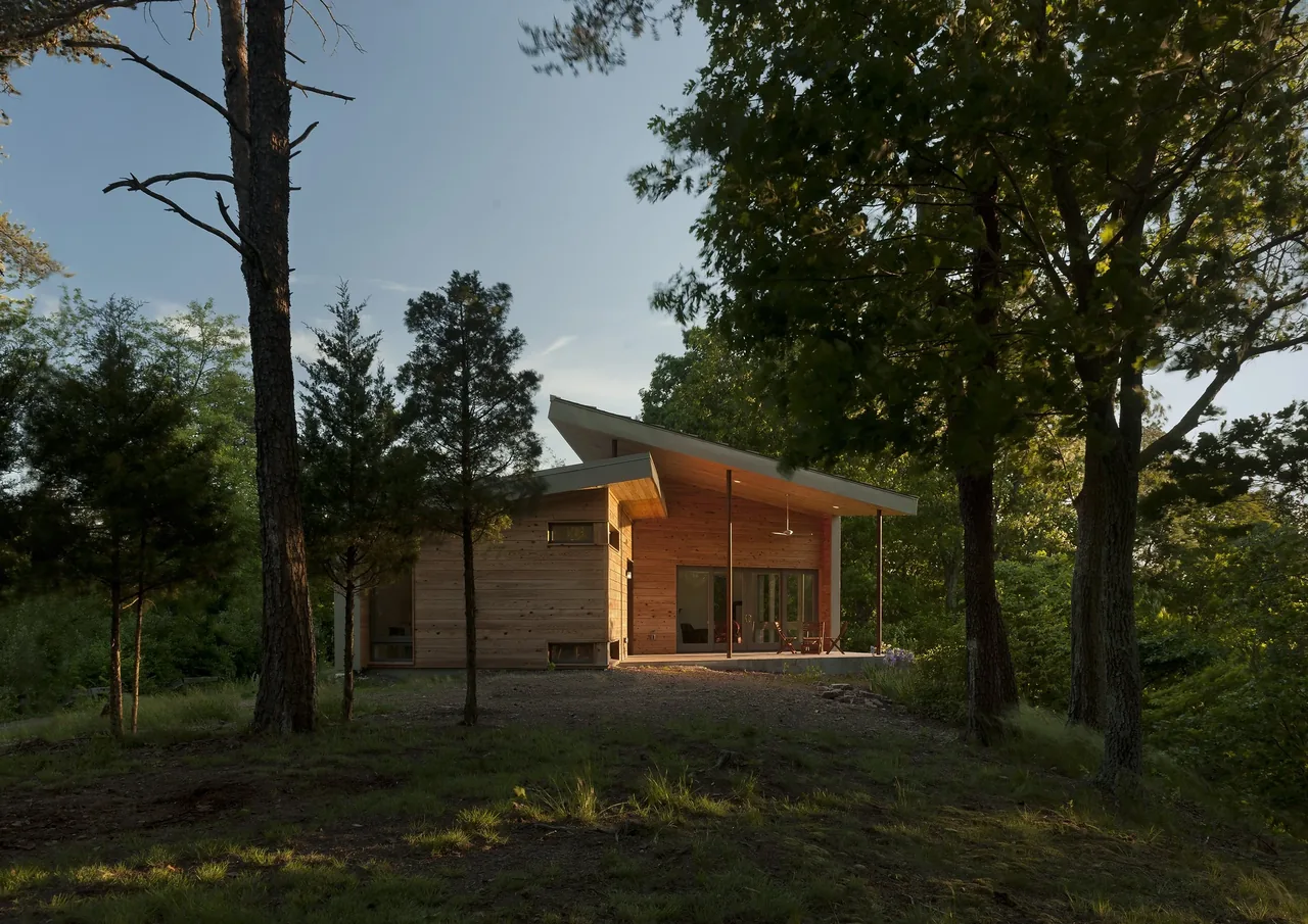 A modern wood house with a shed roof surrounded by trees and grass at sunset.