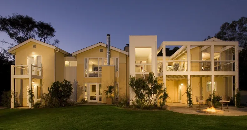 Night view of a modern single-family home with multiple balconies, gable roofs, and outdoor seating around a fire pit.
