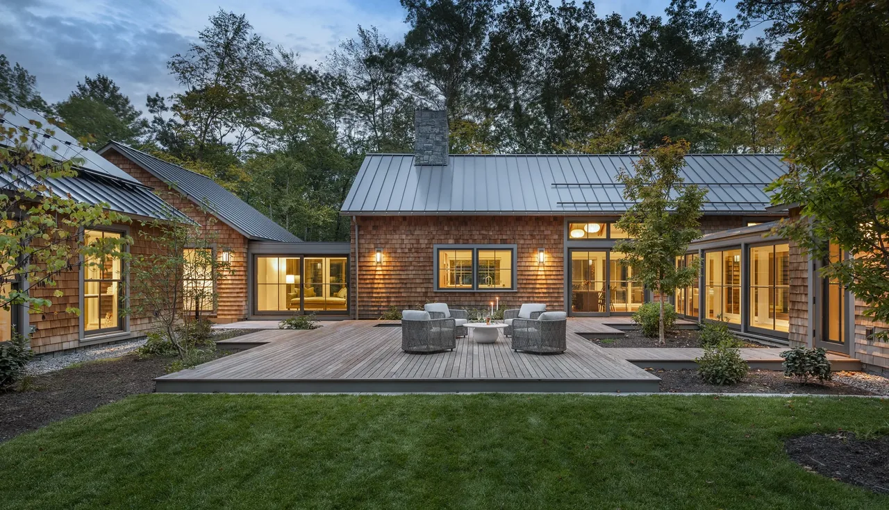 View of a wood-shingled house exterior with a metal roof and a spacious deck with outdoor seating surrounded by trees.