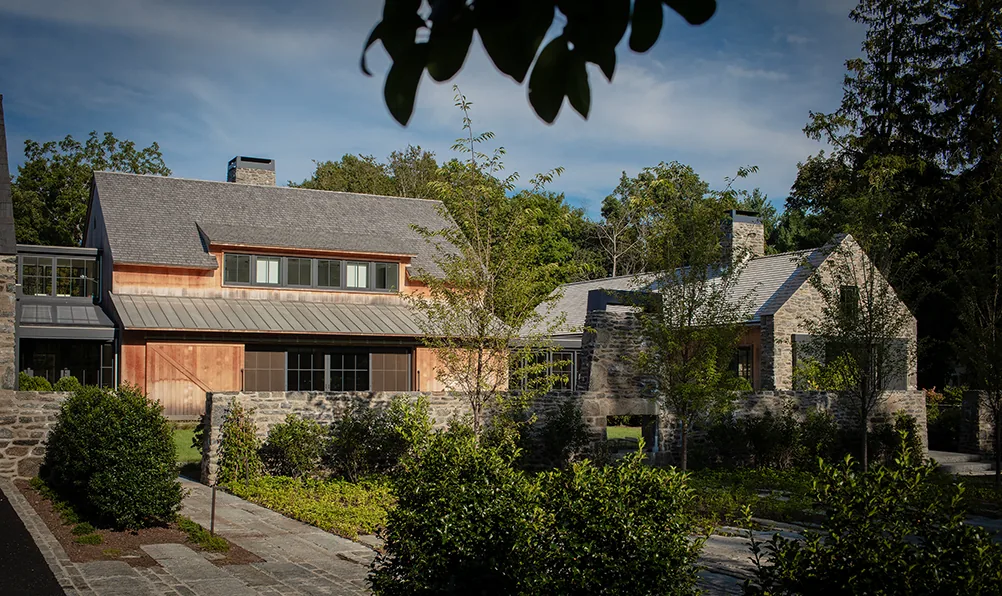 Stone and wood house exterior with chimney and landscaped shrubs under a blue sky.