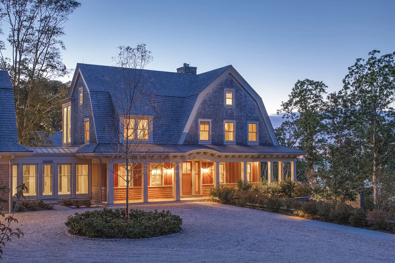 Exterior view of a large farmhouse style home at dusk with lights glowing inside and spaced columns on the porch.