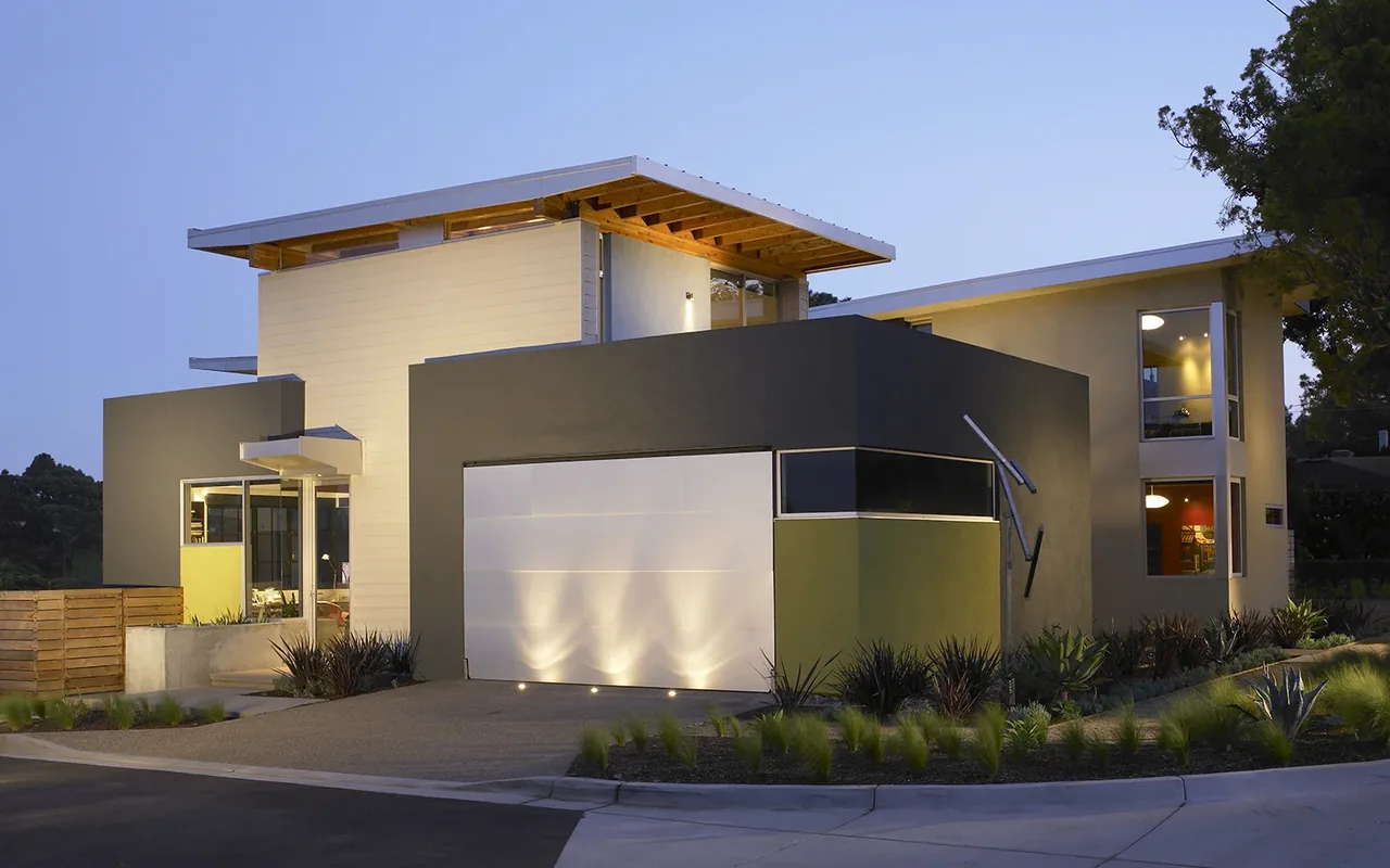 Modern two-story house exterior with flat roofs and a garage at dusk.