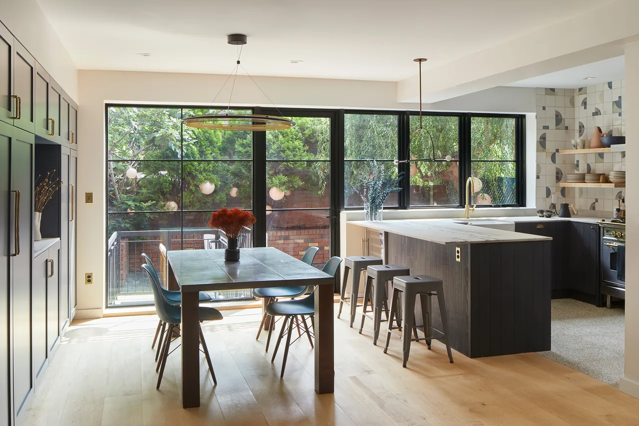 Open kitchen and dining area with large black-framed windows overlooking a garden.