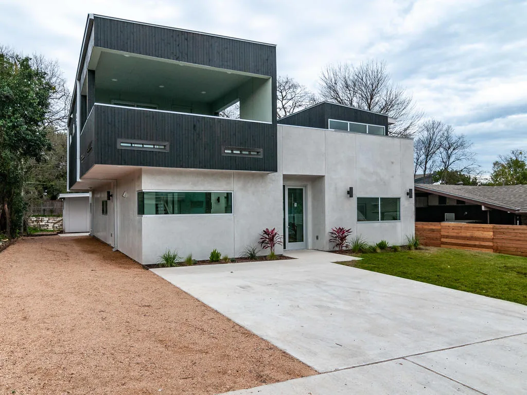 Modern two-story house with white stucco and dark wood siding, featuring a large covered balcony and horizontal windows.