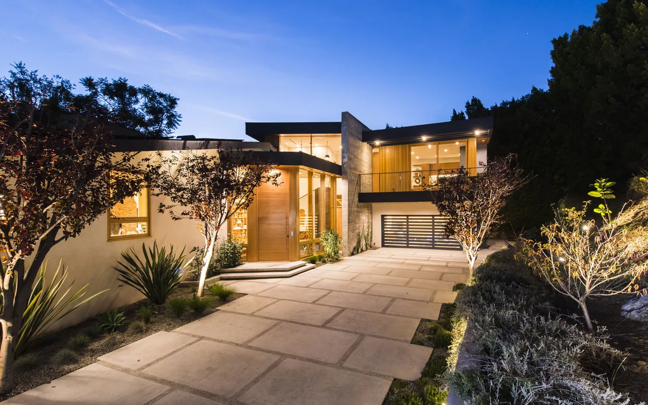 Evening view of modern two-story house with illuminated interior and driveway with concrete slabs.