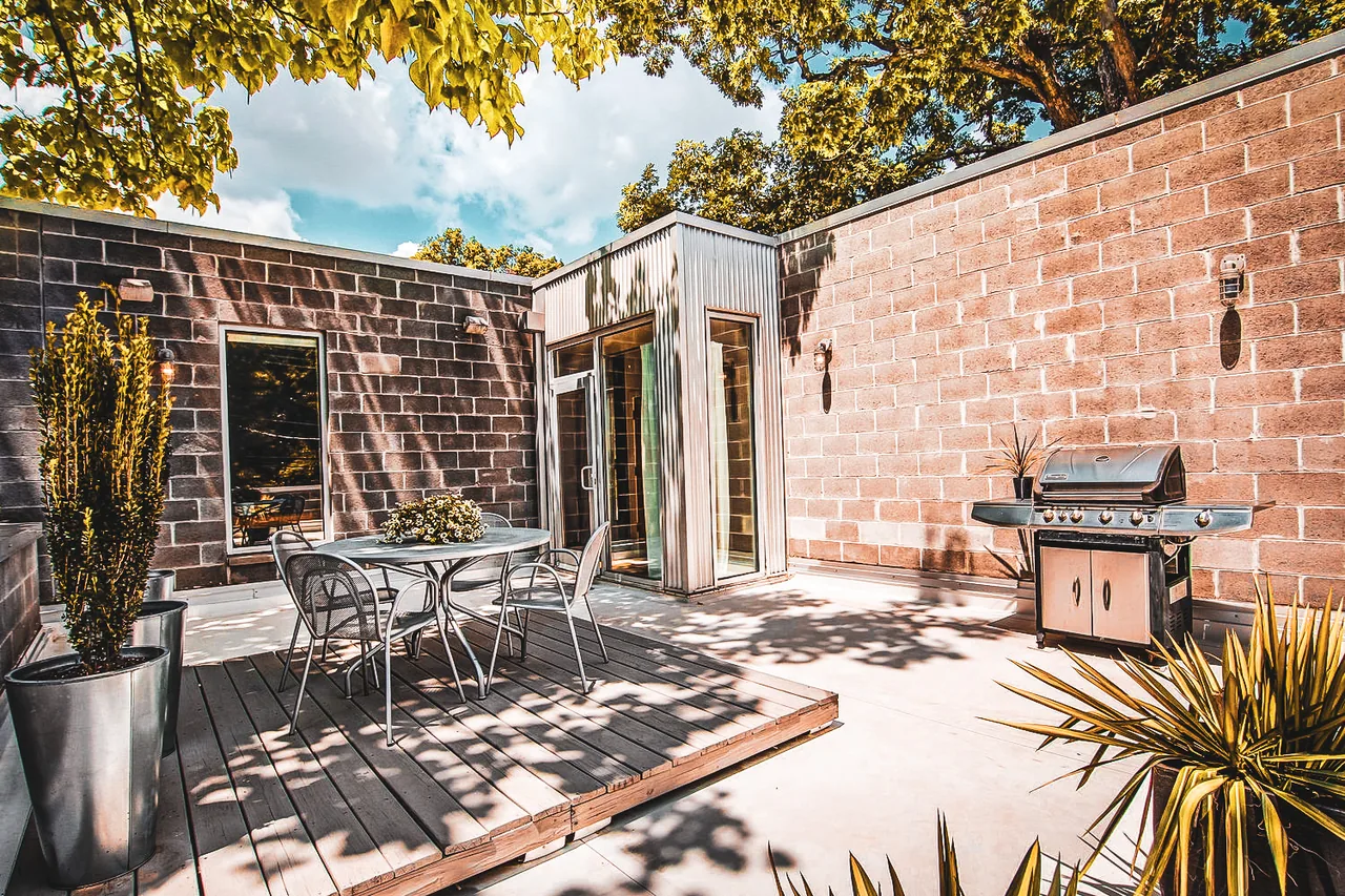 Outdoor patio area with metal patio furniture on a raised wooden deck, surrounded by brick walls and a built-in grill.