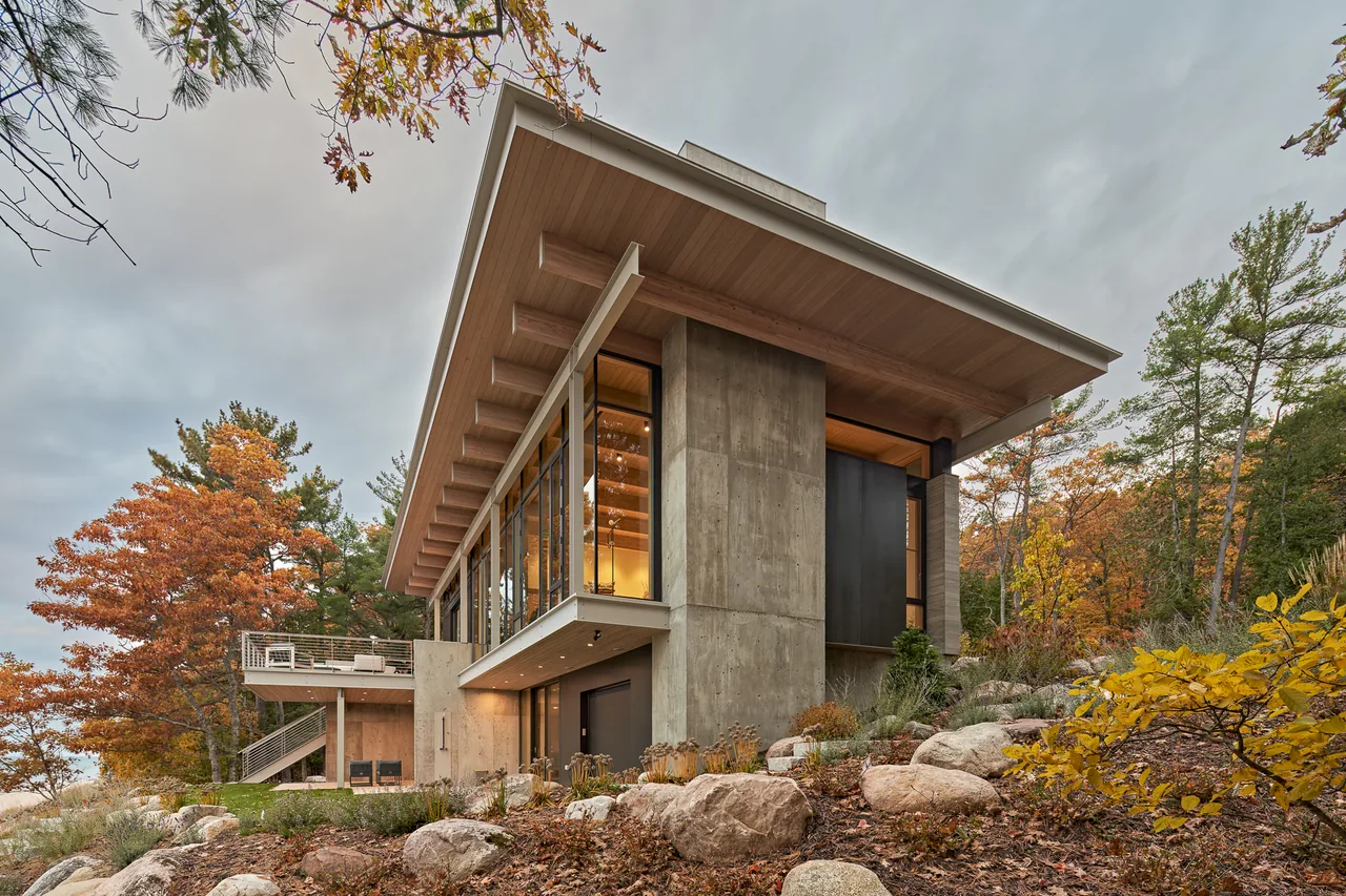 Exterior photo of a modern home perched on a rocky slope with large windows and an overhanging roof.