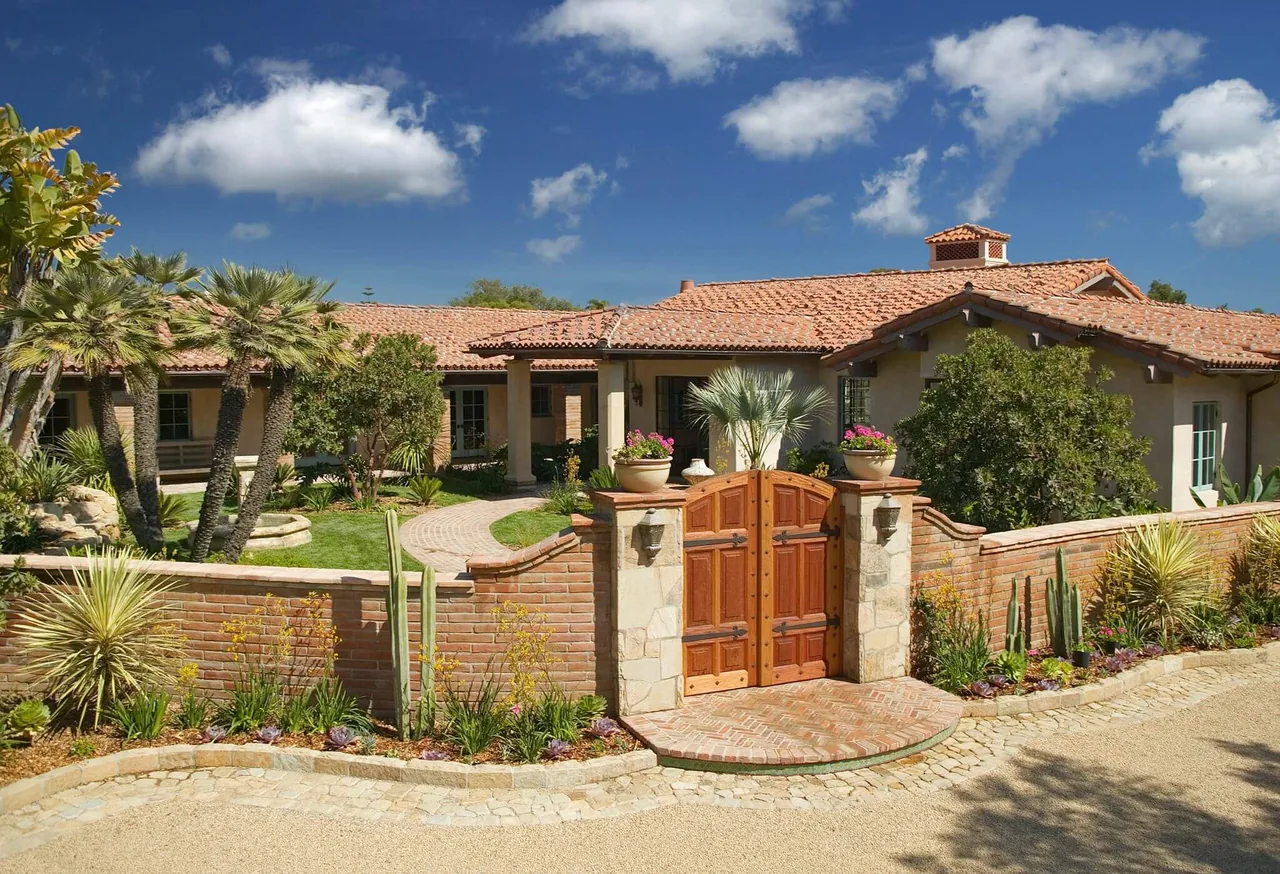 Exterior front view of a one-story estate with terracotta tile roofing and a brick and stone entrance gate.