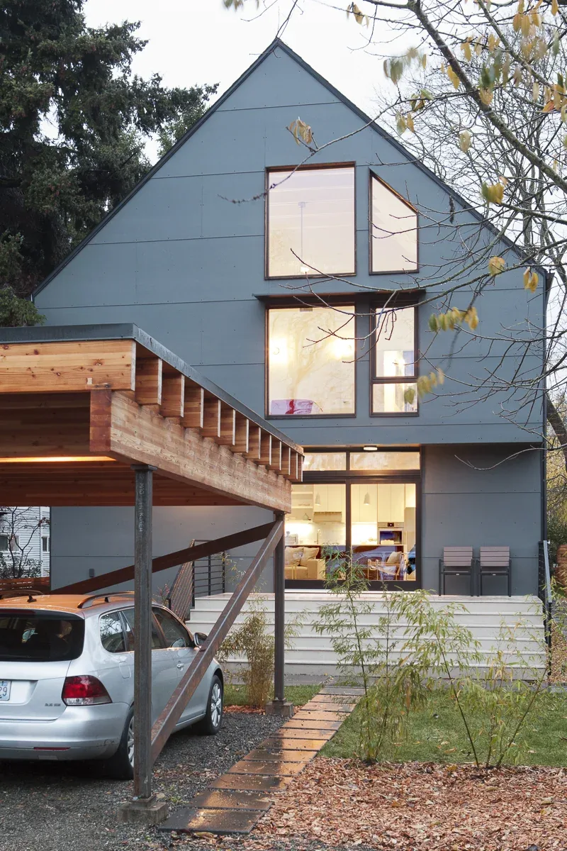 Front view of a modern two-story house with a steep gable roof and a wooden carport on the left.