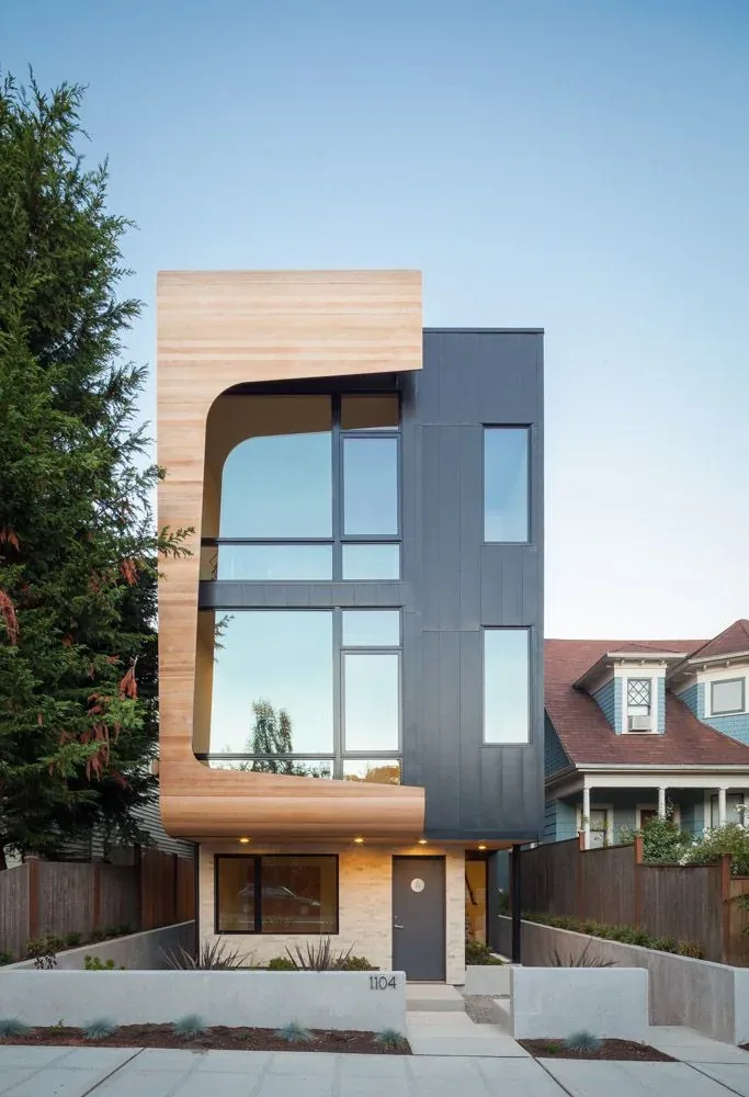 Modern three-story house with large windows and curved wood siding on one side.
