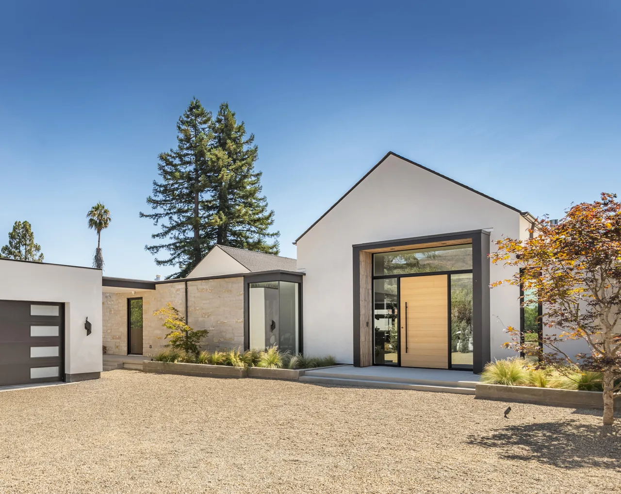 Front exterior view of a modern white house with a large wooden front door and black window frames under a clear blue sky.