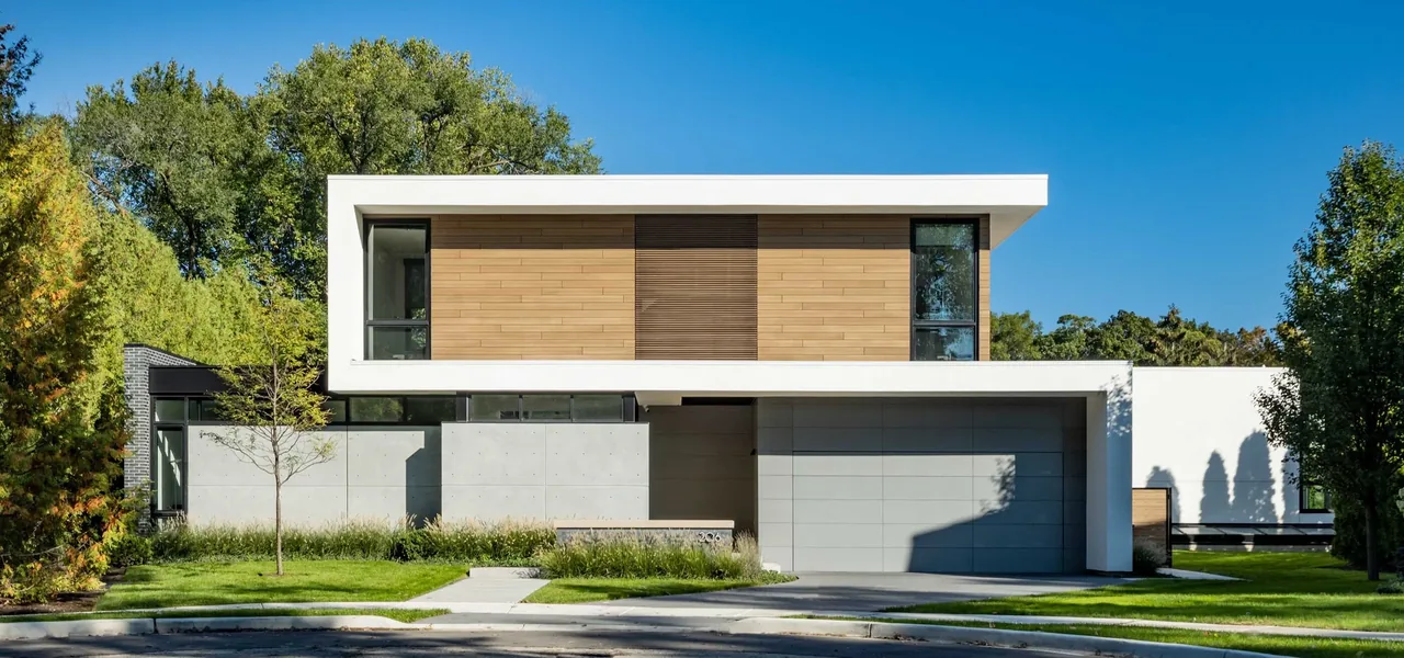 Modern two-story house with wood siding panels and large gray garage door under a flat roof.