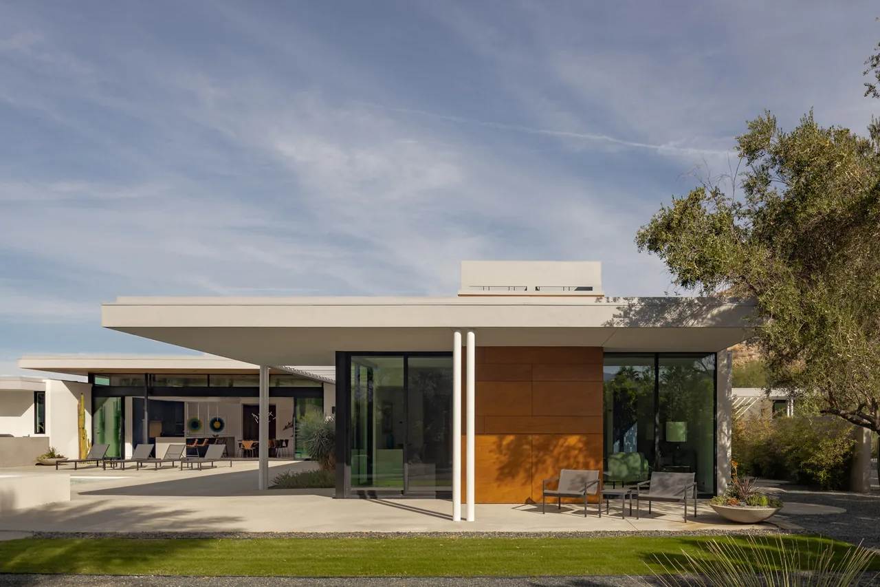 Exterior view of a modern flat-roof house with large glass sliding doors and wooden paneling accent under a clear sky.