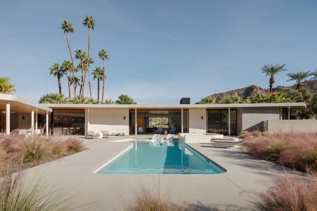Modern single-story home with a central swimming pool and lounge chairs under a clear sky.