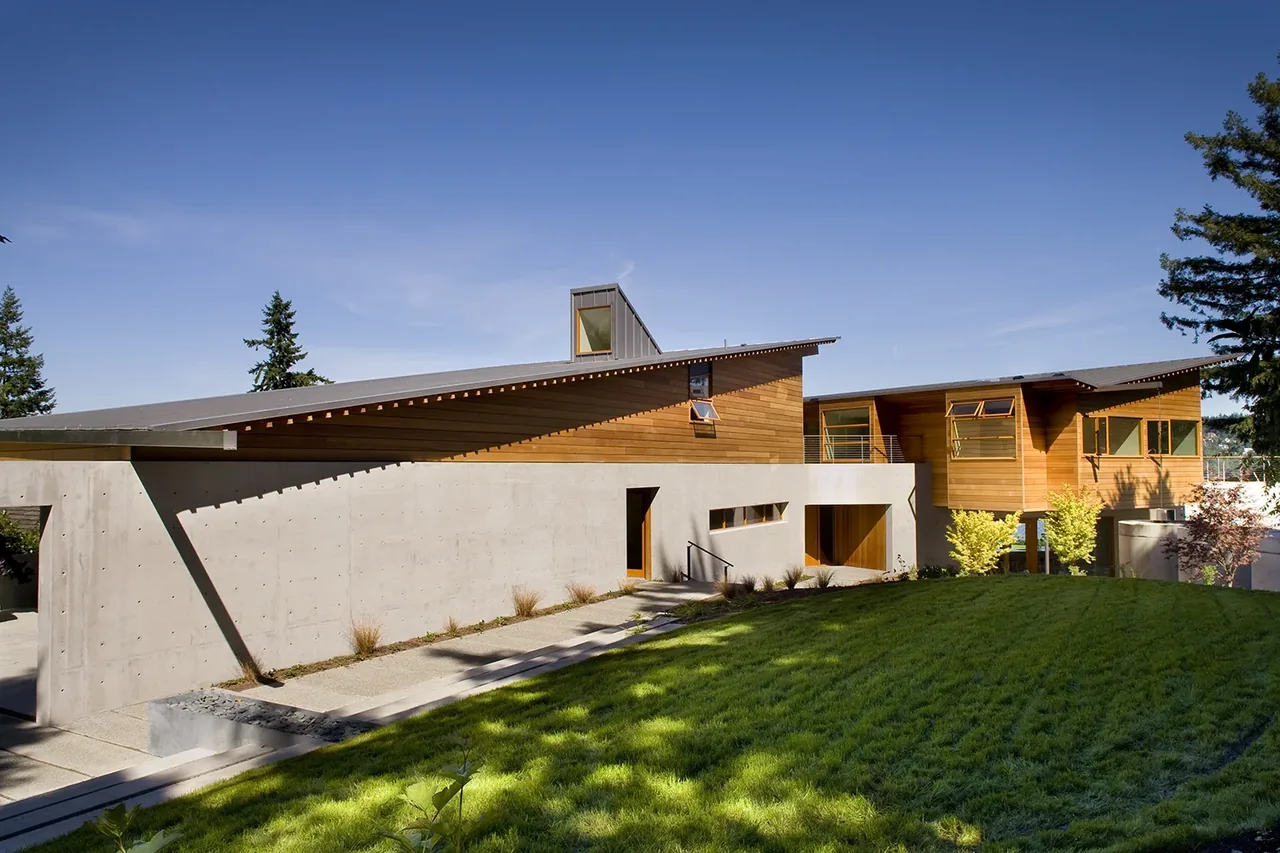 Modern house with concrete base and wooden upper walls under angled metal roofs on a sunny day.