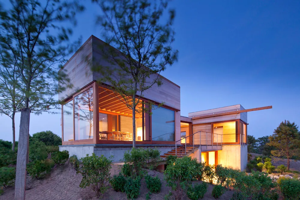 Modern home with large floor-to-ceiling glass windows and warm interior lighting at dusk.