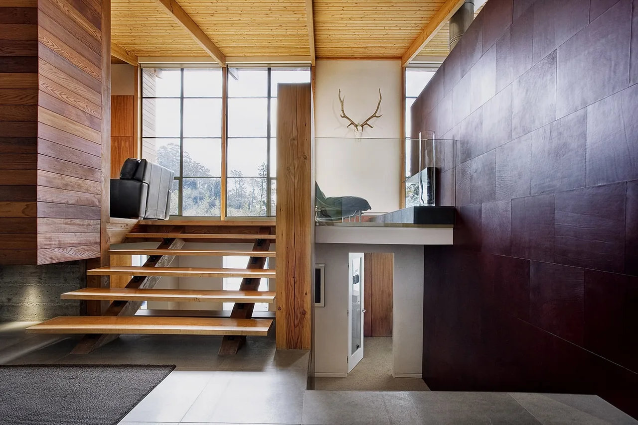 Interior view of a modern home with floating wood stairs, large windows, and a seating area overlooking a staircase.