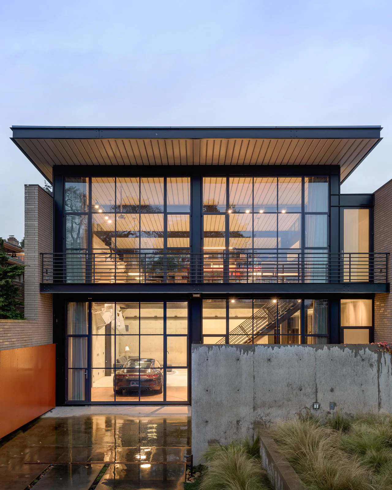 Modern two-story house with large floor-to-ceiling black-framed windows and a cantilevered flat roof at dusk.