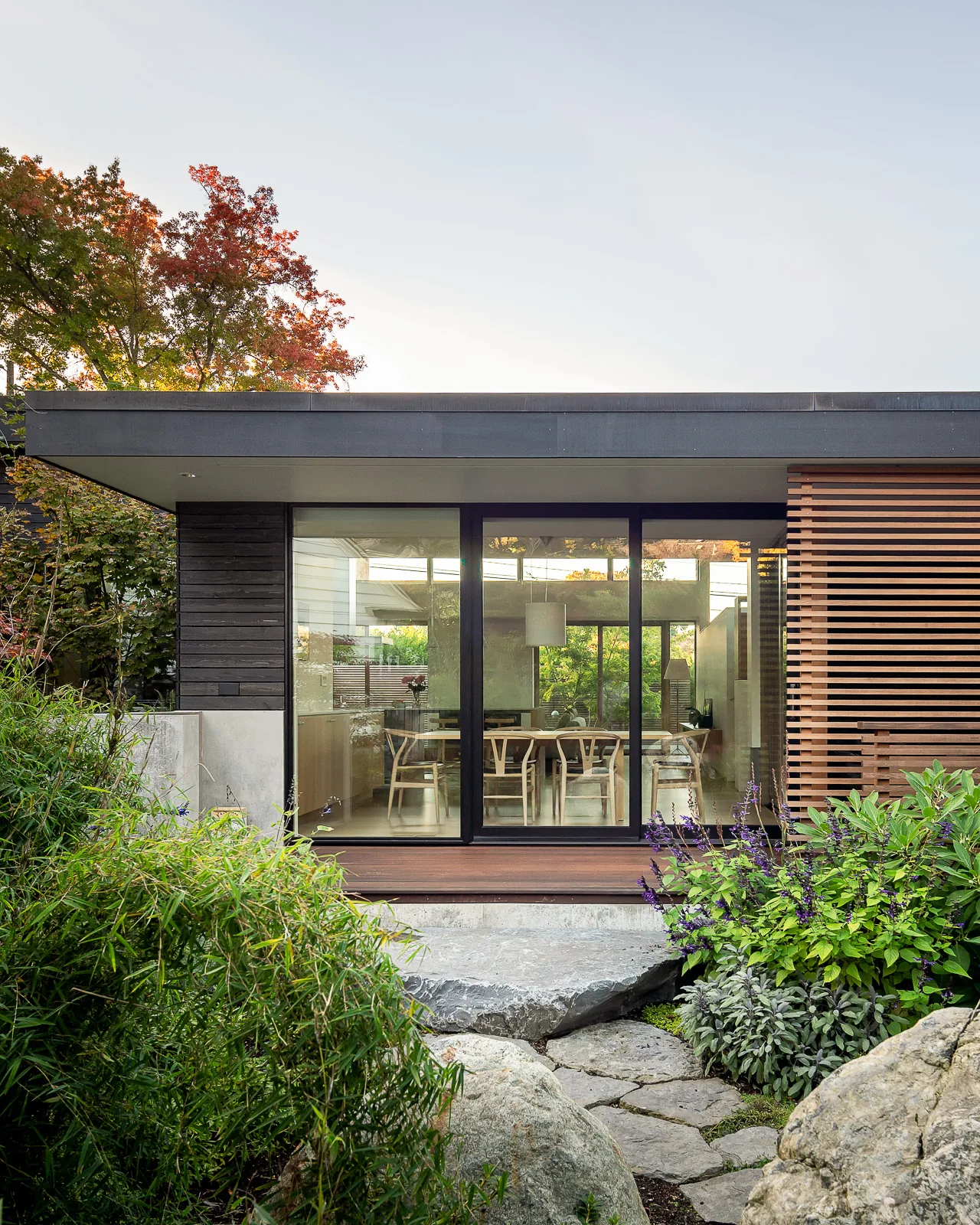 Modern single-story house exterior with large glass sliding doors leading to a dining area and landscaped garden path.