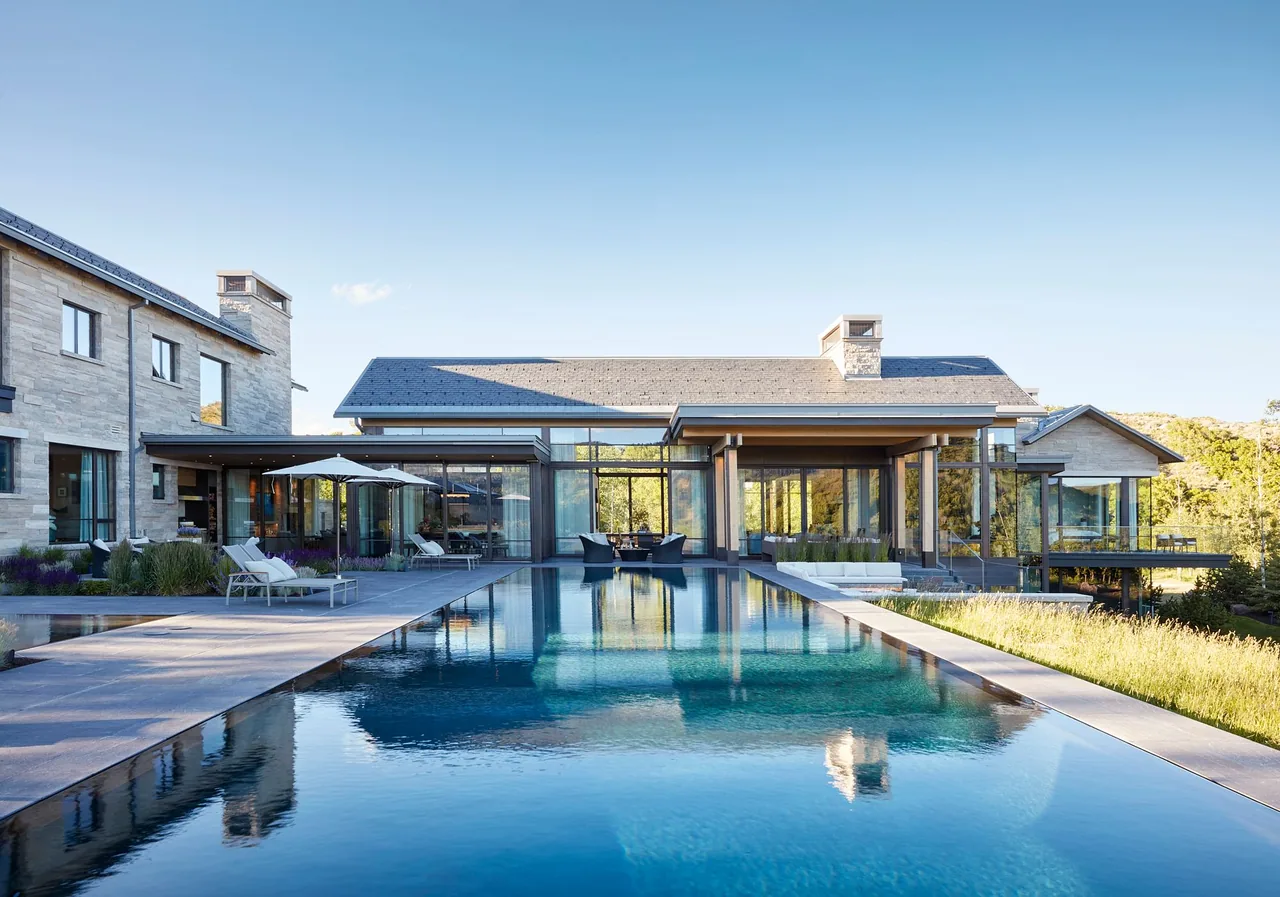 Modern large residence with an outdoor infinity-edge pool reflecting the building on a clear day.