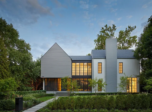 Front exterior view of Phillips Park House with large windows and a central chimney at dusk.