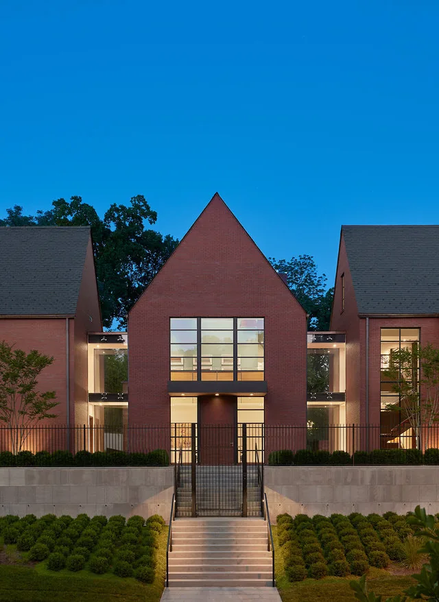 Front exterior view of a brick residential building with steep gable roofs and large grid windows at dusk.