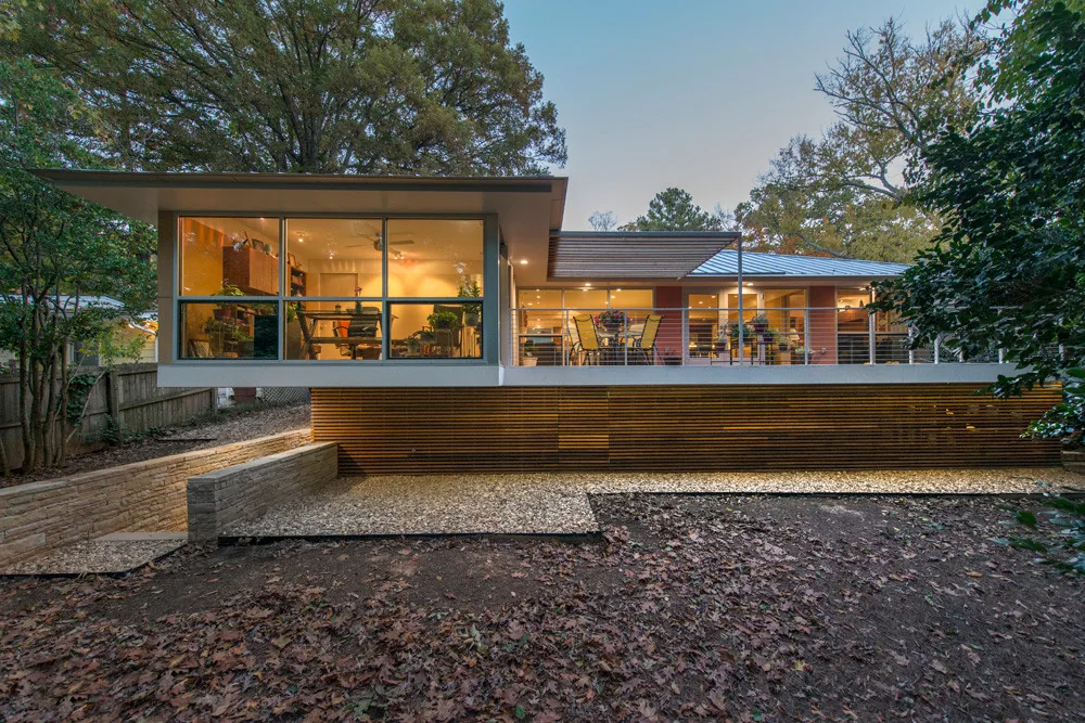 Modern house exterior in wooded yard with large glass windows and raised deck with outdoor seating